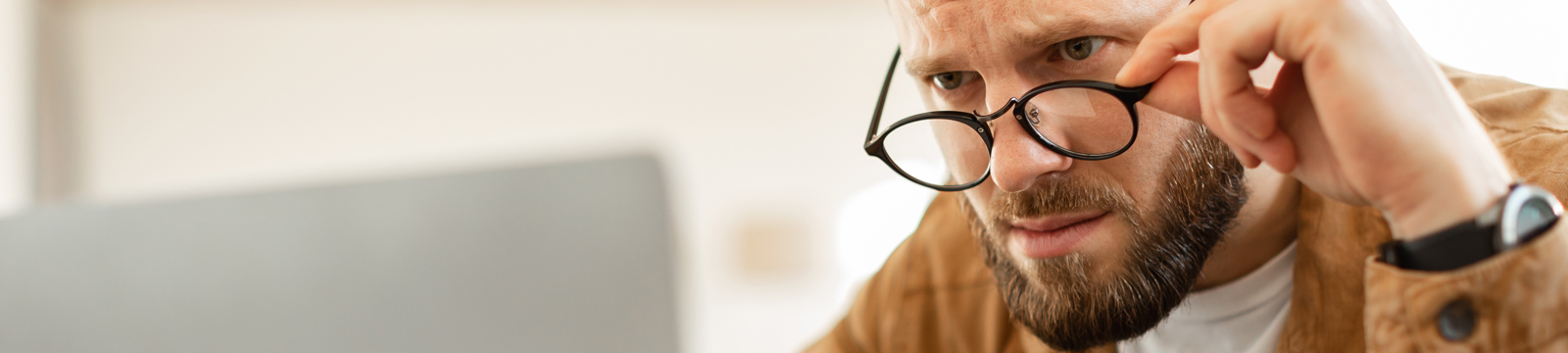 Man looking perplexed at laptop screen over top of his glasses